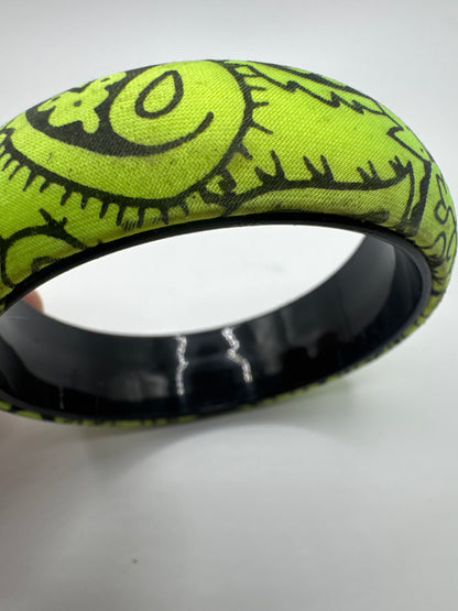 Wide lime green bangle bracelet featuring a black doodle-style line art pattern